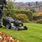 Gardener mowing an autumn lawn beside a clipped hedge in Keighley