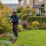 Gardener tending shrubs beside a lawn and established flower border