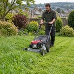 Gardener cutting long grass in a residential garden.