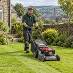 Gardener mowing a Keighley garden lawn bordered by shrubs and stone walls.