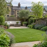 Yorkshire stone terrace garden with a paved patio, seating, lawn and planted borders.